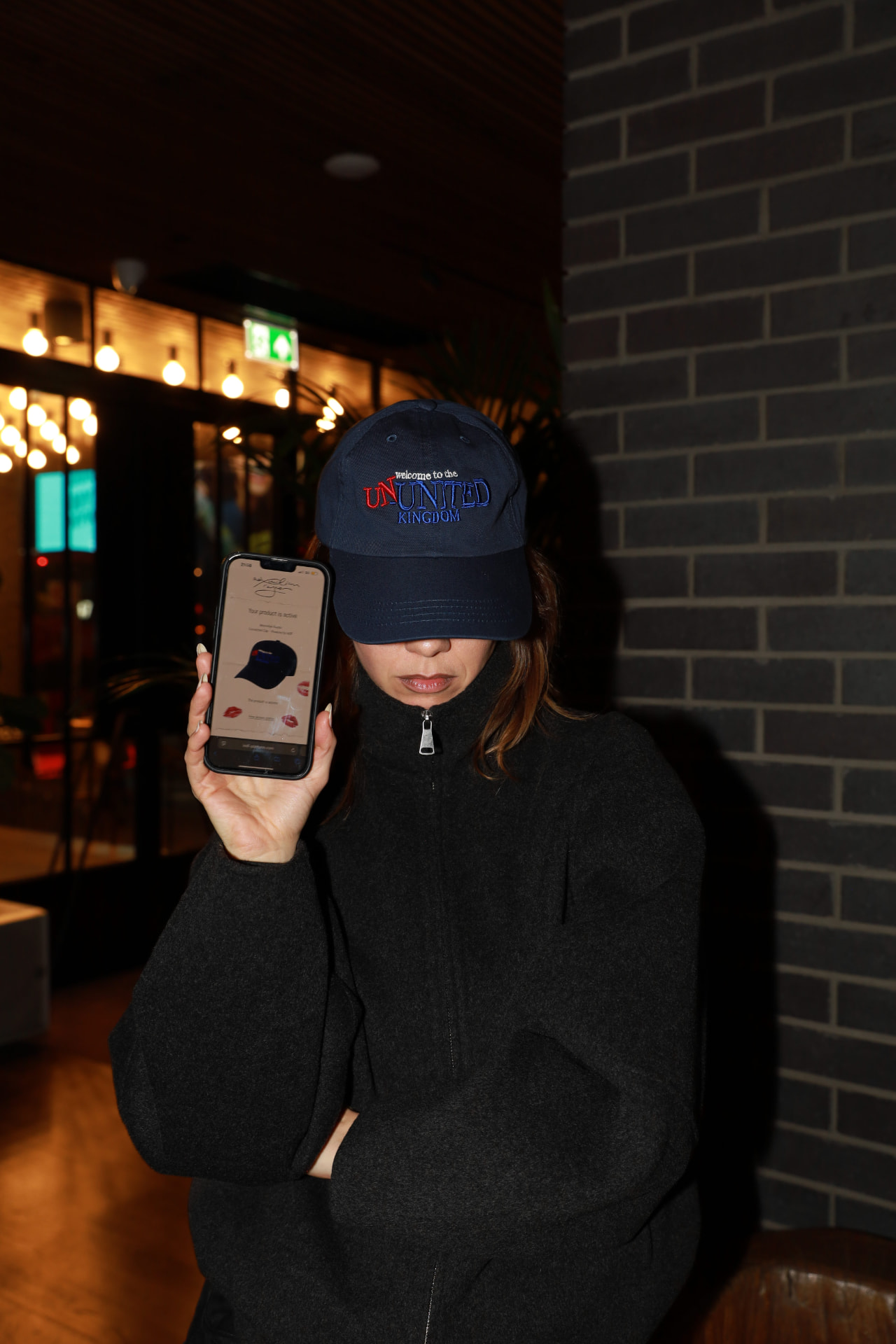 Guest holding a phone showing the active product record beside the navy connected cap